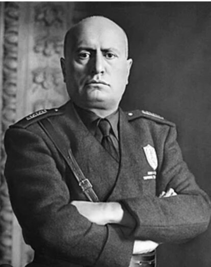 Black-and-white portrait of a stern male military officer with arms crossed and a badge on his chest.
